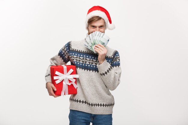 young beard man holding a christmas gift box and money on white