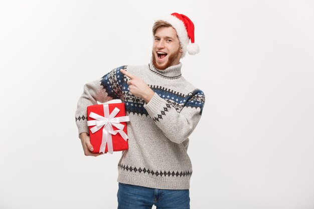 Young beard man in sweater holding box and pointing hand at side