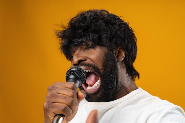 Young bearded african american man singing in microphone against yellow background