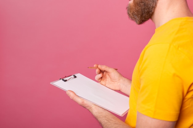 Abbigliamento casual uomo giovane barbuto dipendente prendere appunti su uno sfondo rosa