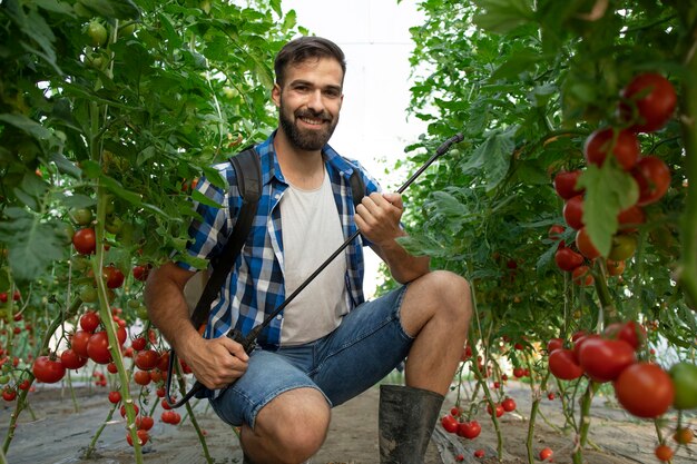Молодой бородатый фермер опрыскивает растения пестицидами для защиты от болезней