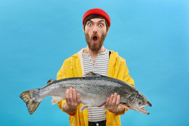 young bearded fisherman holding big sea-water fresh-caught fish in both hands