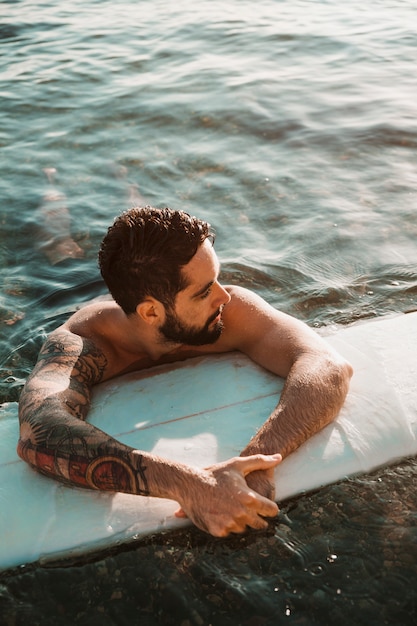 Young bearded guy lying on surf board in water