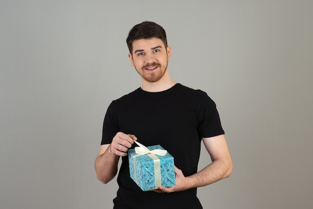 Young bearded guy trying to open present on a grey.