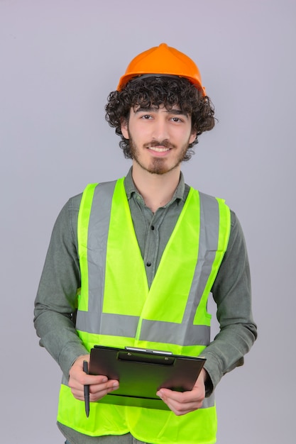 Young bearded handsome engineer holding clipboard and pen in hands with smile on face over isolated white wall