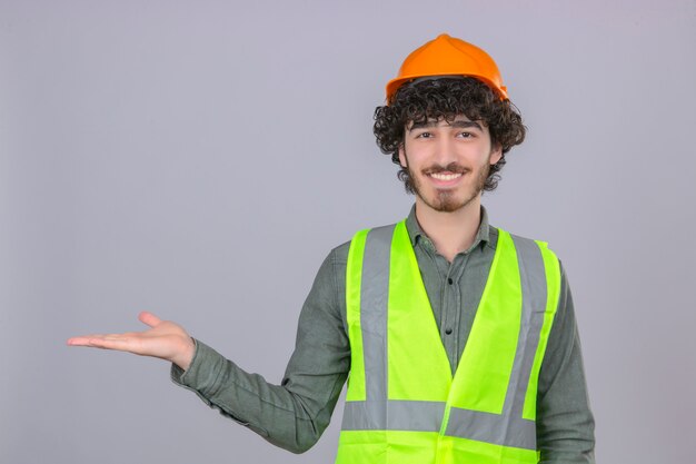 Young bearded handsome engineer smiling cheerful presenting copy space and pointing with palm of hand looking at the camera over isolated white wall