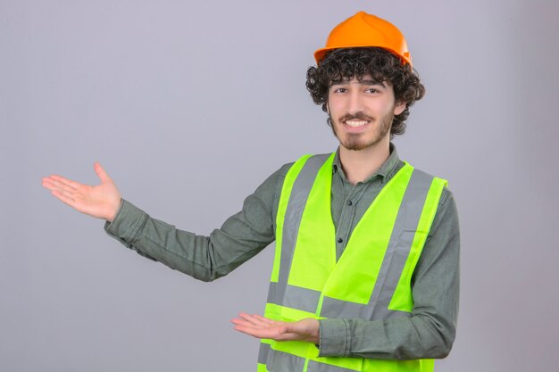 Young bearded handsome engineer smiling cheerful presenting and pointing with palm of hand looking at the camera over isolated white wall