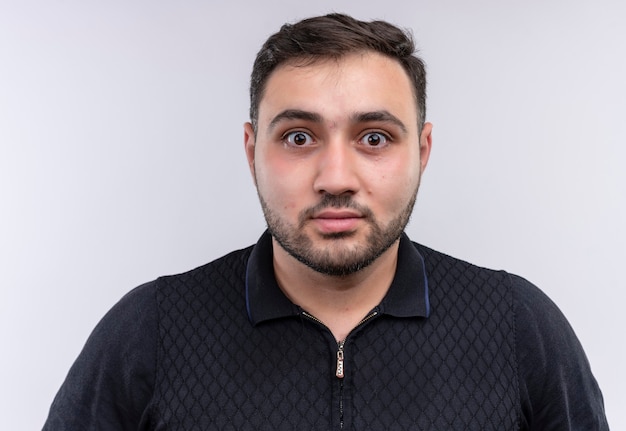 Young bearded man in black shirt looking at camera surprised 