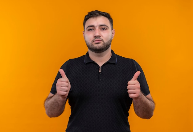 Young bearded man in black shirt  looking confident showing thumbs up with both hands 