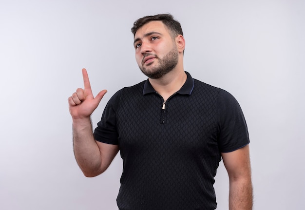 Young bearded man in black shirt pointing finger up trying to remember 