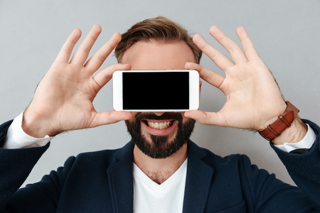 Free photo young bearded man cover face with smartphone with blank screen