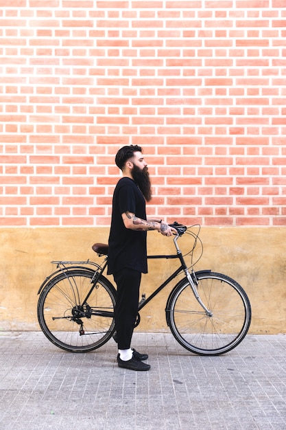 彼の自転車を屋外に立っている間コーヒーを飲む若いアゴヒゲ