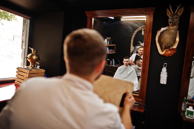 Foto gratuita giovane uomo barbuto che si fa tagliare i capelli dal parrucchiere mentre è seduto su una sedia al barbiere barber soul