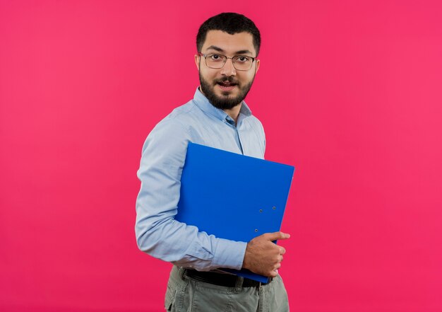 眼鏡と青いシャツの若いひげを生やした男が顔に笑顔でフォルダーを保持