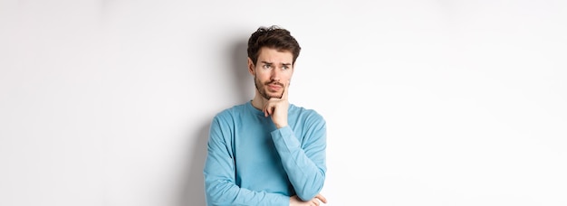 Free photo young bearded man looking pensive and frowning thinking about problem or trouble standing worried ag