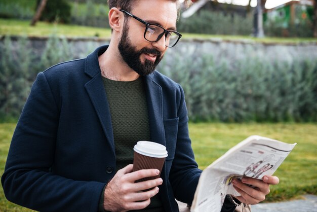 young bearded man sitting outdoors reading newspaper