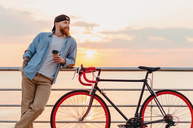 夕焼けの海で自転車で旅行する若いひげを生やした男