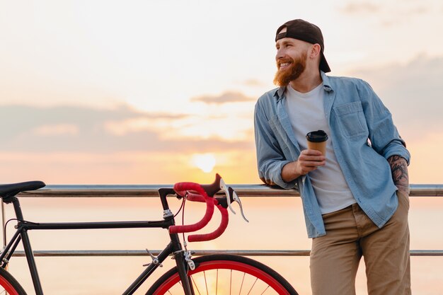 夕焼けの海で自転車で旅行する若いひげを生やした男