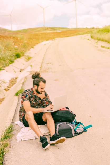 Young bearded man using laptop sitting on road