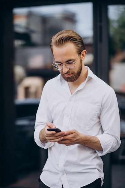 Young bearded man using phone and walking at the street