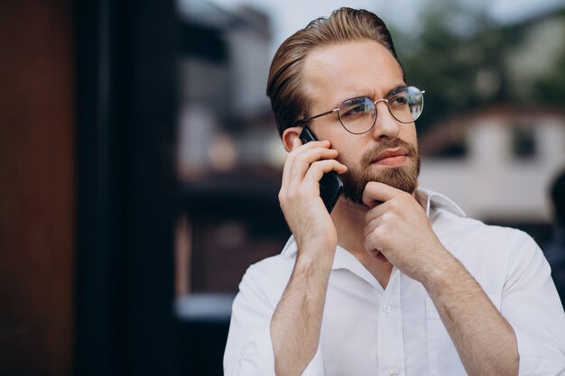 電話を使用して通りを歩いている若いひげを生やした男