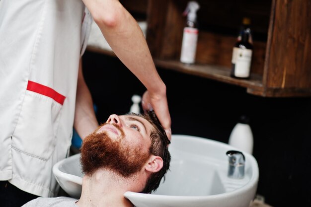 Young bearded man washing head by hairdresser while sitting in chair at barbershop Barber soul