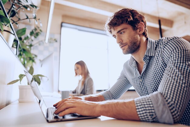 Young bearded successful businessman working on laptop in office with female colleague