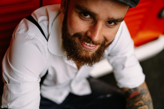 Young bearded tattooed man portrait close-up. A romantic guy in a white shirt, cap and suspenders. Peaky Blinders. old-fashioned, retro.