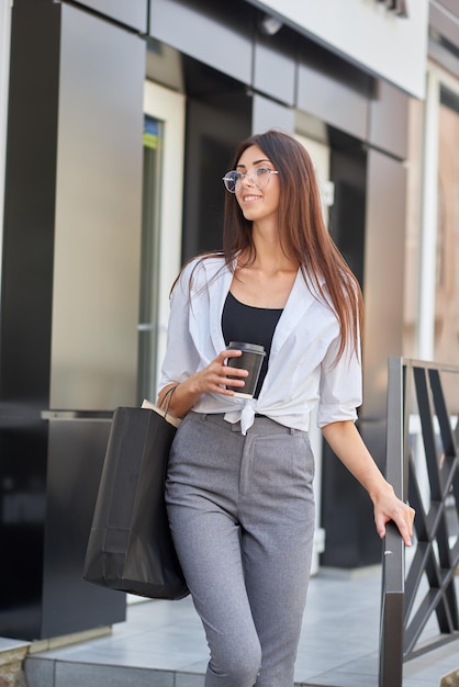 Young beatiful girl carrying paper bags going out from shop