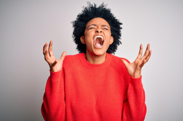 Free photo young beautiful african american afro woman with curly hair wearing red casual sweater celebrating mad and crazy for success with arms raised and closed eyes screaming excited winner concept