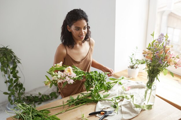 白い壁に職場で花の世話をする若いアフリカ美女花屋。