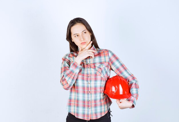 Young beautiful architect woman holding security helmet over white wall. 