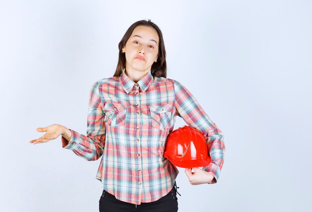 Young beautiful architect woman holding security helmet over white wall. 