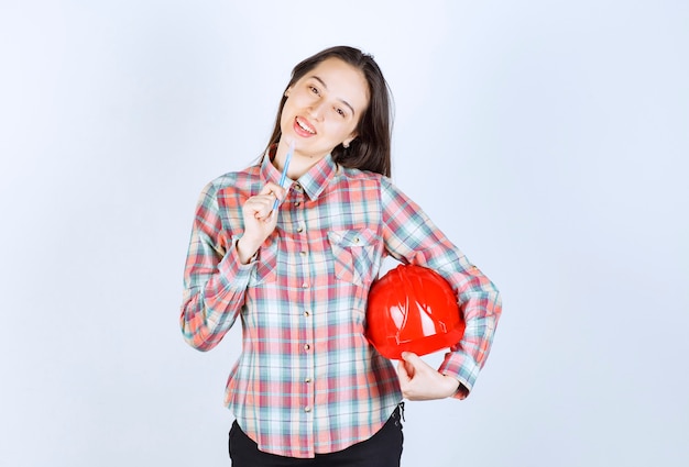 Foto gratuita giovane bella donna dell'architetto che tiene il casco di sicurezza con la penna.