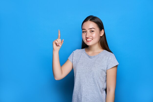 若い美しいアジア人の笑顔と青い壁に親指を表示