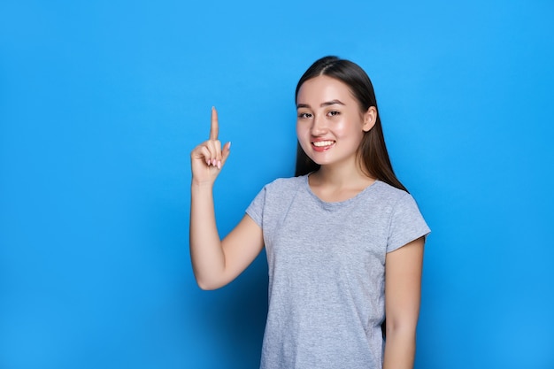 Молодая красивая азиатка улыбается и показывает палец вверх на синей стене