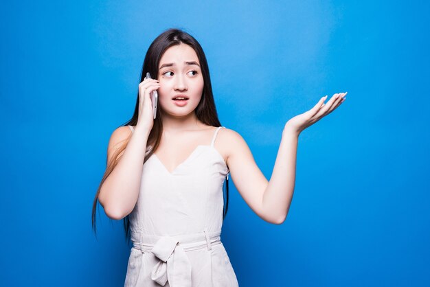 Young beautiful asian woman having conversation talking on smartphone isolated over blue wall