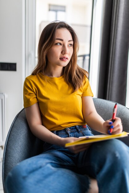 Free photo young beautiful asian woman relaxing in living room at home, reading books in the morning