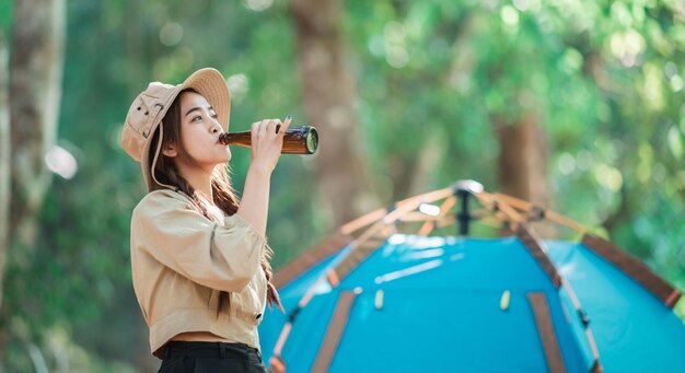 Молодые красивые азиатские женщины и друзья-путешественники отдыхают перед палаткой для кемпинга. Им нравится разговаривать и пить пиво, весело и счастливо вместе.