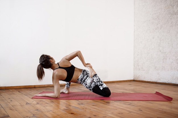 Giovane bella donna atletica che si esercita in yoga dell'interno sulla stuoia rossa