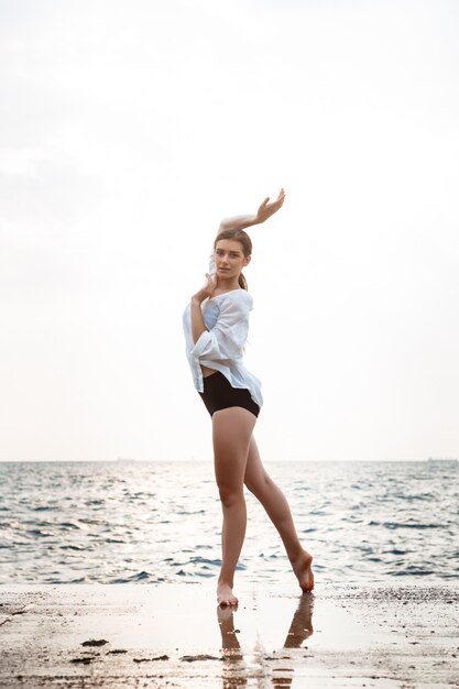 Молодая красивая балерина танцует и позирует снаружи, морская стена