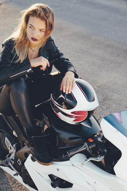 バイクのポーズに座っている若い美しいバイカー女性