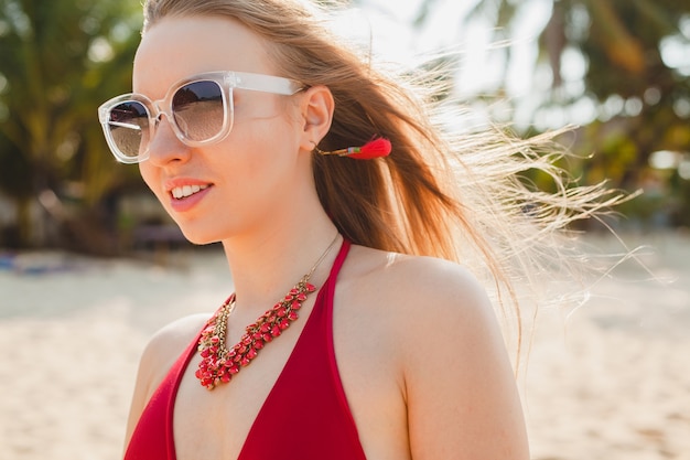 Young beautiful blond woman sunbathing on beach in red swimming suit, sunglasses