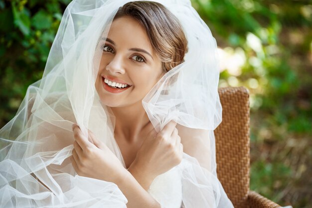 Young beautiful blonde bride in wedding dress and veil smiling.