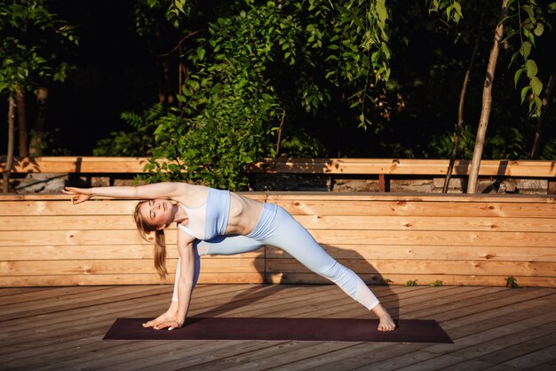 Young beautiful blonde girl practicing yoga outside at sunrise.