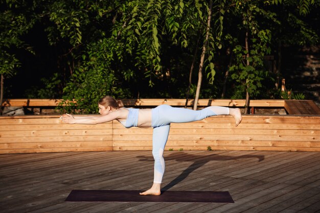 Young beautiful blonde girl practicing yoga outside at sunrise.