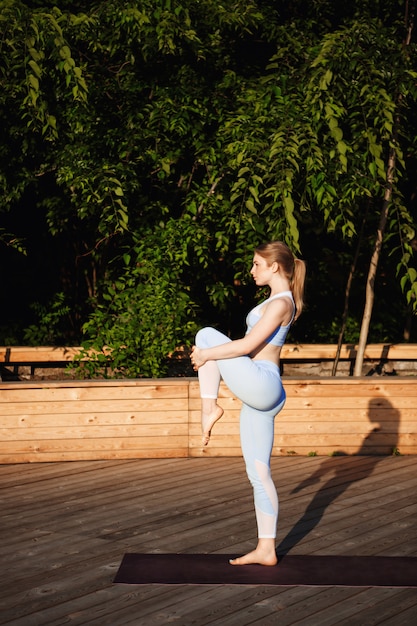 Young beautiful blonde girl practicing yoga outside at sunrise.