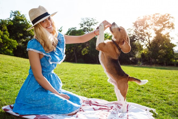 Young beautiful blonde girl walking, playing with beagle dog in park.