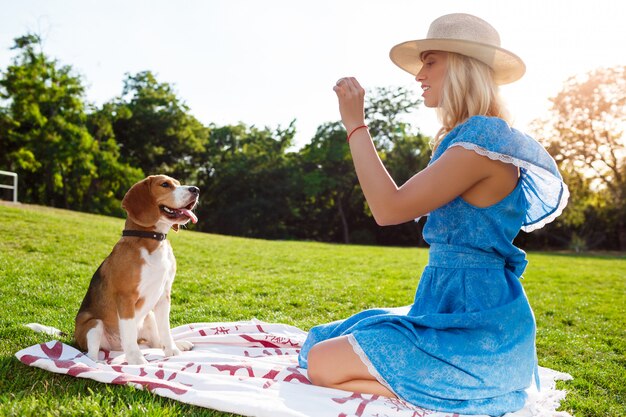 Young beautiful blonde girl walking, playing with beagle dog in park.