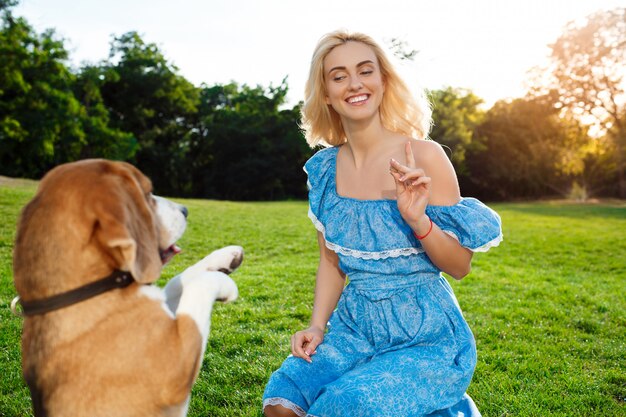 ウォーキング、公園でビーグル犬と遊ぶ若い美しいブロンドの女の子。